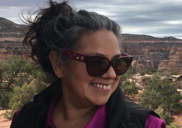 Image of woman in purple shirt and black vest smiling with sunglasses.